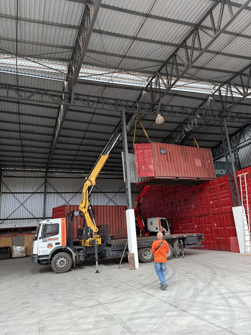 Caminhão munck da Trans Mineirinho descarregando contêiner dentro de galpão industrial