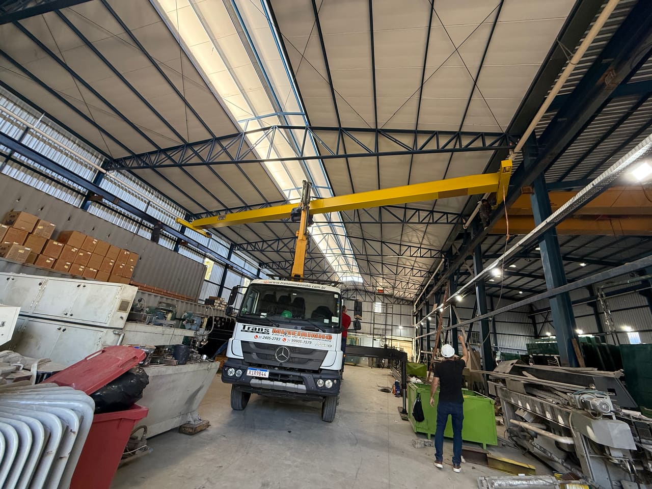 Caminhão munck operando dentro de fábrica sob ponte rolante